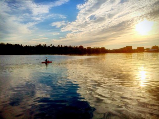 Lone kayaker immersed in the gold of a sunset with a city view on the horizon.